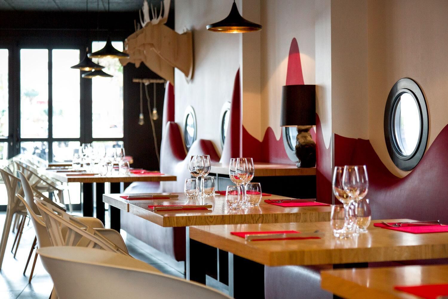 Interior de restaurante con mesas de madera, servilletas rojas y copas de vino.