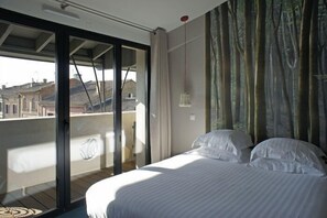 Un dormitorio con una cama grande, vistas a un balcón exterior a través de una puerta corredera, y un mural temático de bosque.