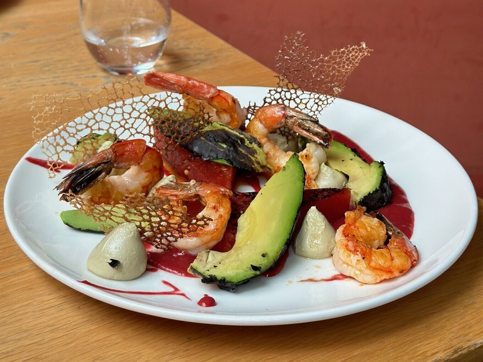A seafood dish on a white plate with a glass of water on a wooden table.