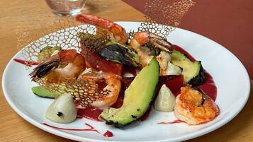 A seafood dish on a white plate with a glass of water on a wooden table.