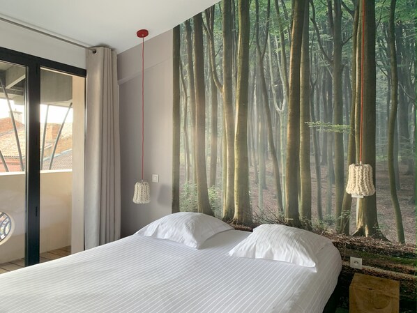 Un dormitorio con una cama grande, un mural de un bosque en la pared y vistas al exterior a través de una puerta corrediza.