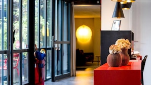 Eine moderne Hotelhalle mit großen Glasüren, einem roten Empfangsbereich und zwei Vasen mit Blumen.