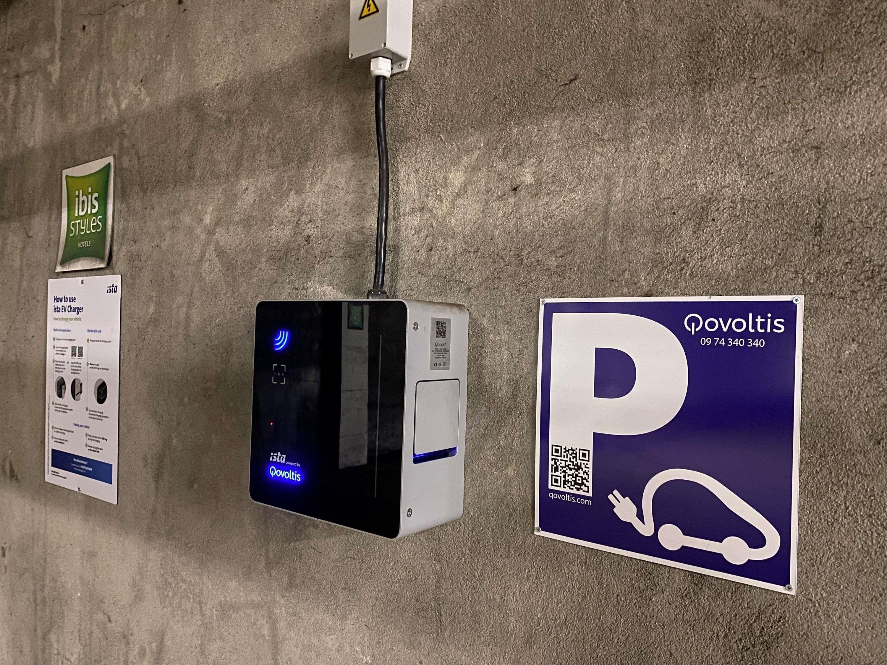 Una estación de carga, un cartel con un código QR y un cartel para 'ibis Styles Hotels'.