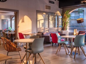 A modern indoor seating area with tables and chairs, a large window, and a plant. - ibis Styles Blois Centre Gare (Blois)