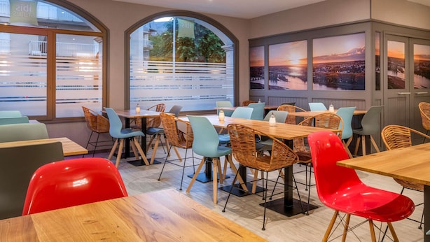 A dining area with tables and chairs, large windows with views, and a cityscape painting on the wall. - ibis Styles Blois Centre Gare (Blois)