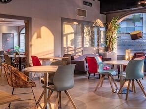 Un espace de détente intérieur moderne, avec des tables et des chaises, une grande fenêtre et une plante.