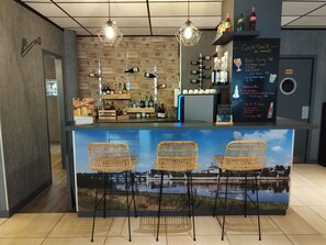 Un espace bar avec des chaises en osier, un comptoir où sont exposées des bouteilles et un menu écrit à la craie.