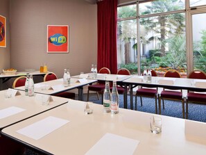 A conference room with tables, chairs, water bottles, and a view of palm trees through large windows.