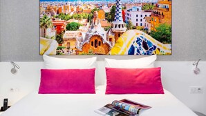 A hotel room with a bed, two pillows, a magazine, and a large cityscape painting on the wall. - ibis Styles Blois Centre Gare (Blois)