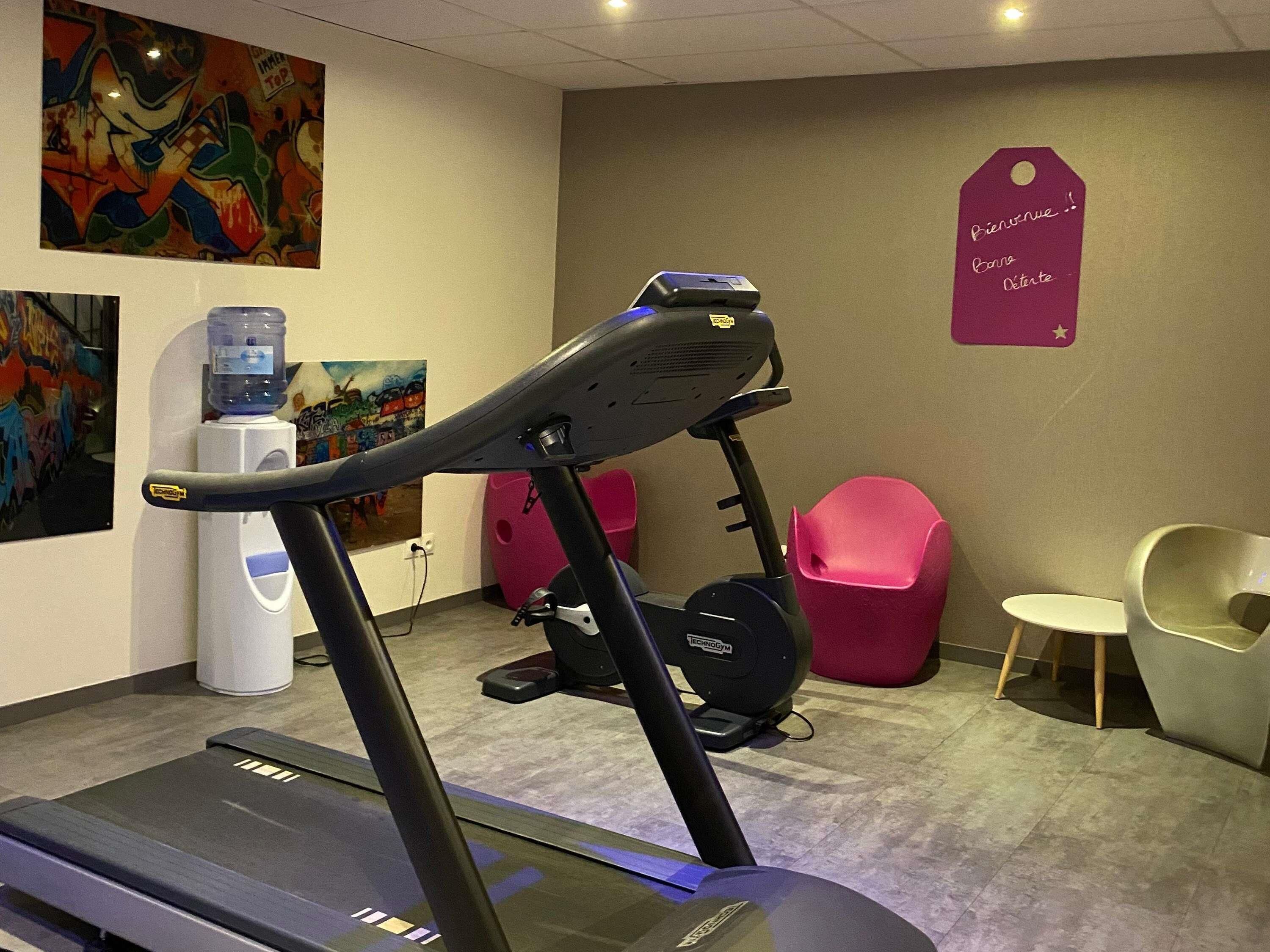 Een sportschool met trainingsapparatuur, een waterdispenser en een muur met een kleurrijke muurschildering.