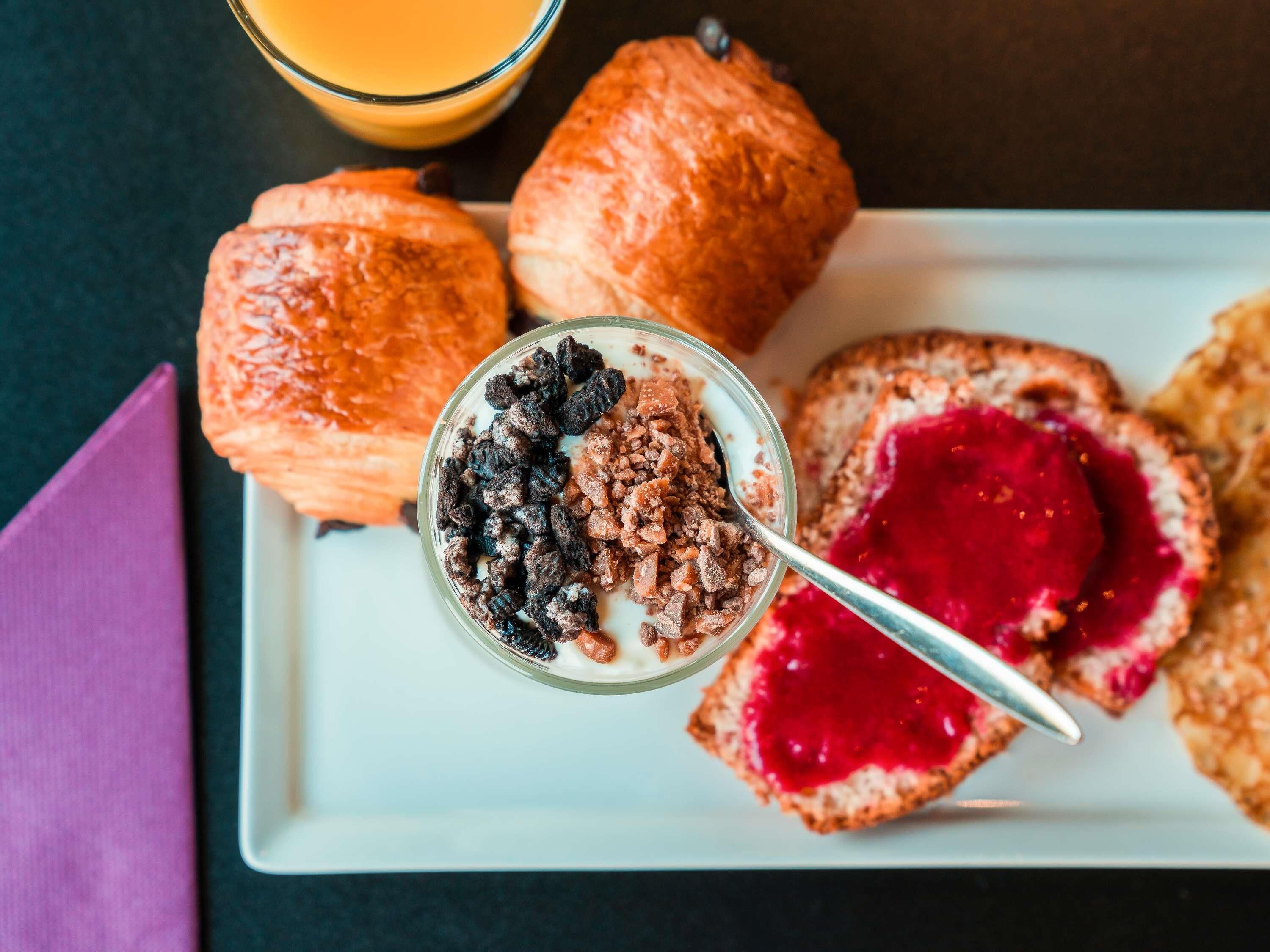 A breakfast plate with pastries, a glass of orange juice, and a bowl of cereal with milk and toppings.