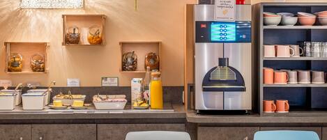 A modern café with a self-service beverage station, a variety of food options, and a seating area with a table and chairs.