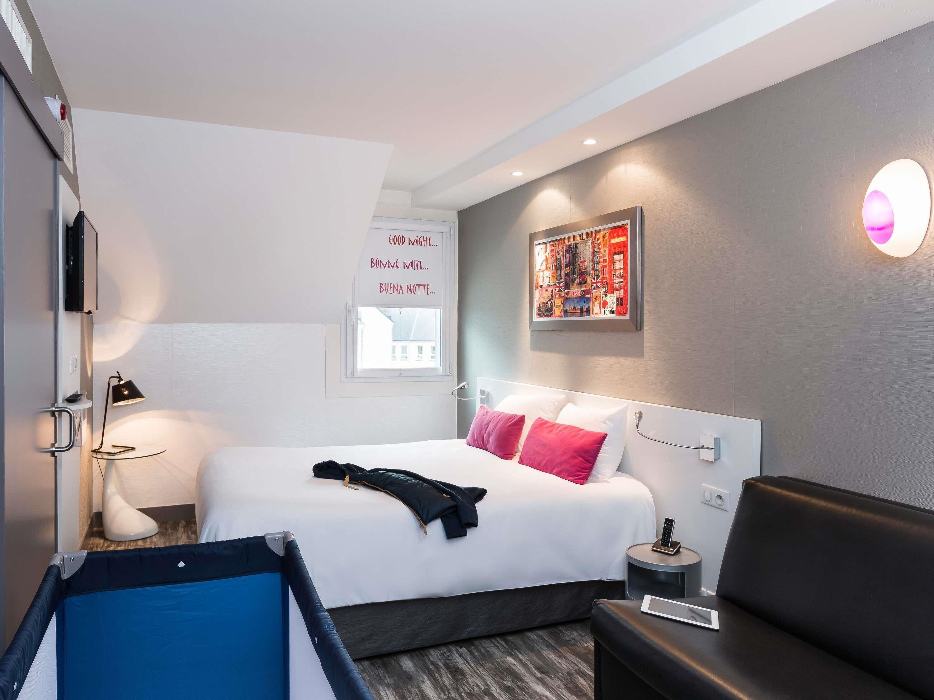 A modern hotel room with a bed, bedside table, lamp, and a framed picture on the wall.