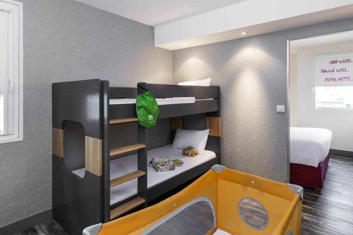 A bunk bed with a green bag, a playpen, and a window with multilingual wall art.