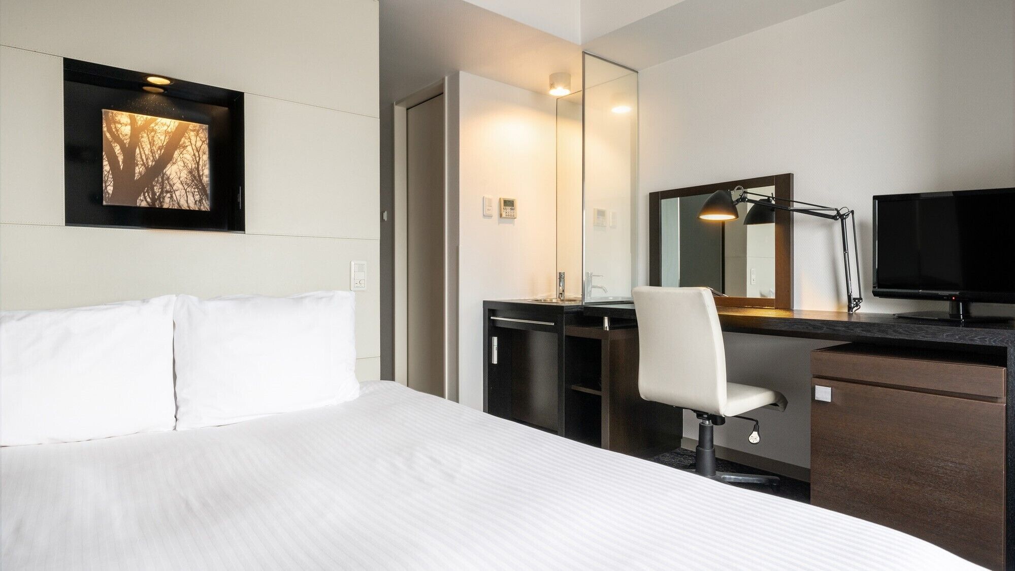 A hotel room with a bed, a desk with a chair, a television, and a mirror.