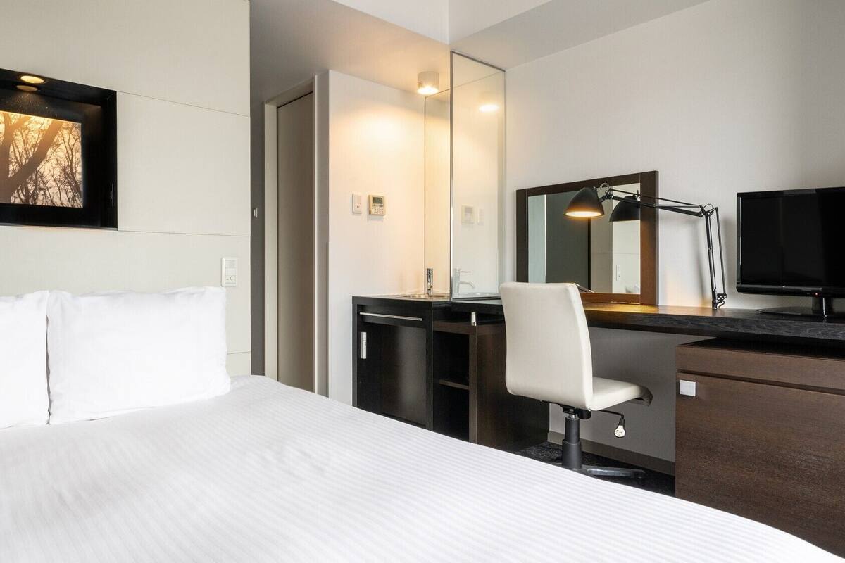 Ein Hotelzimmer mit Bett, Schreibtisch mit Stuhl, Fernseher und Spiegel.