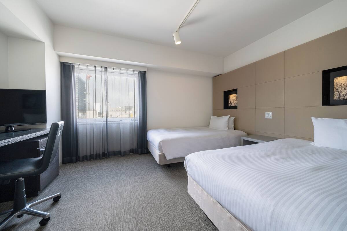 A hotel room with a bed, a desk, a chair, a TV, and a window with curtains.