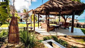 A thatched-roof gazebo with wooden benches and tables, surrounded by a pool and greenery. - Moriah Natal Beach Hotel (Natal)