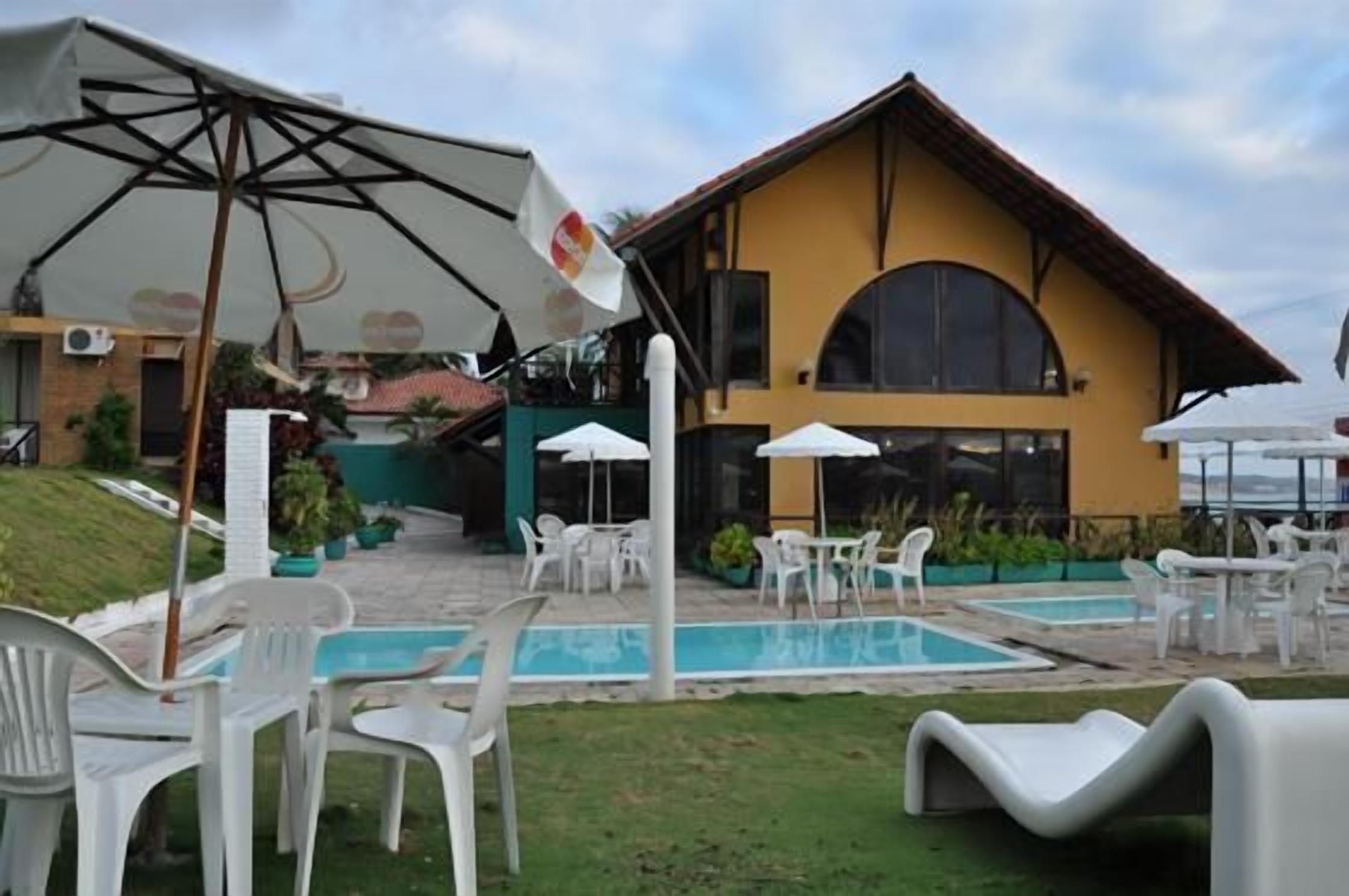 A hotel with outdoor seating, a swimming pool, and a yellow building with a large arched window.