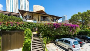 A building with a stone facade, a wooden staircase leading to a balcony, and a parking area with cars. - Divi Divi Praia Hotel (Natal)