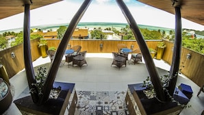 A covered outdoor seating area with a view of the ocean, featuring wicker furniture and potted plants. - Divi Divi Praia Hotel (Natal)