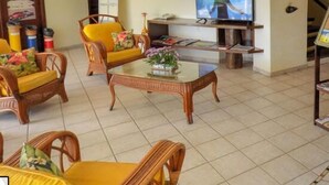 A living room with wicker furniture, a glass coffee table, and a flat-screen TV. - Divi Divi Praia Hotel (Natal)