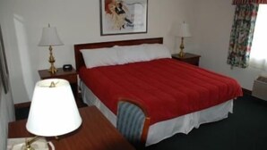 Habitación de hotel con una cama, dos mesitas de noche con lámparas, un reloj de pared y un cuadro enmarcado.