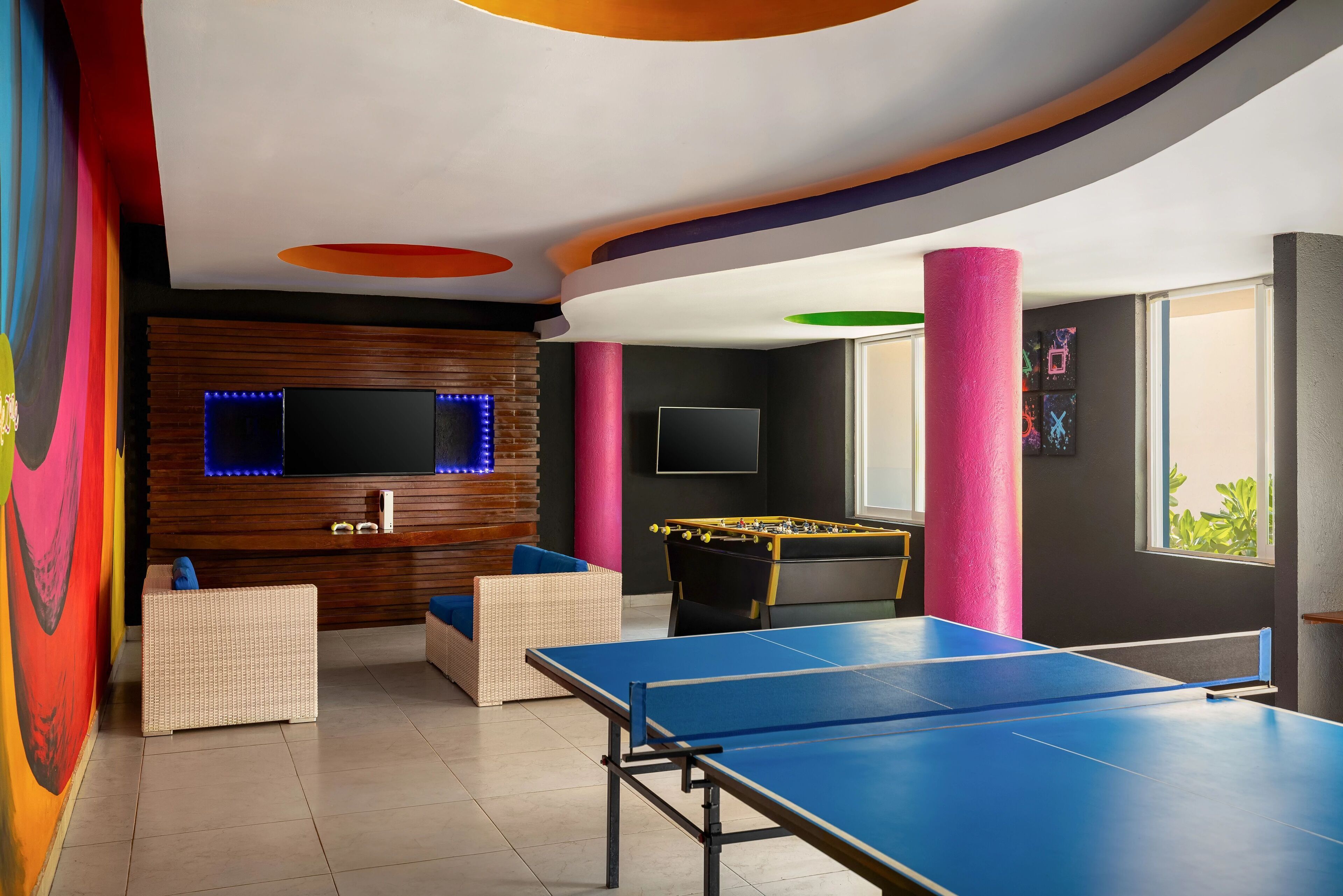 A room with a foosball table, a ping pong table, a TV, and a sofa.