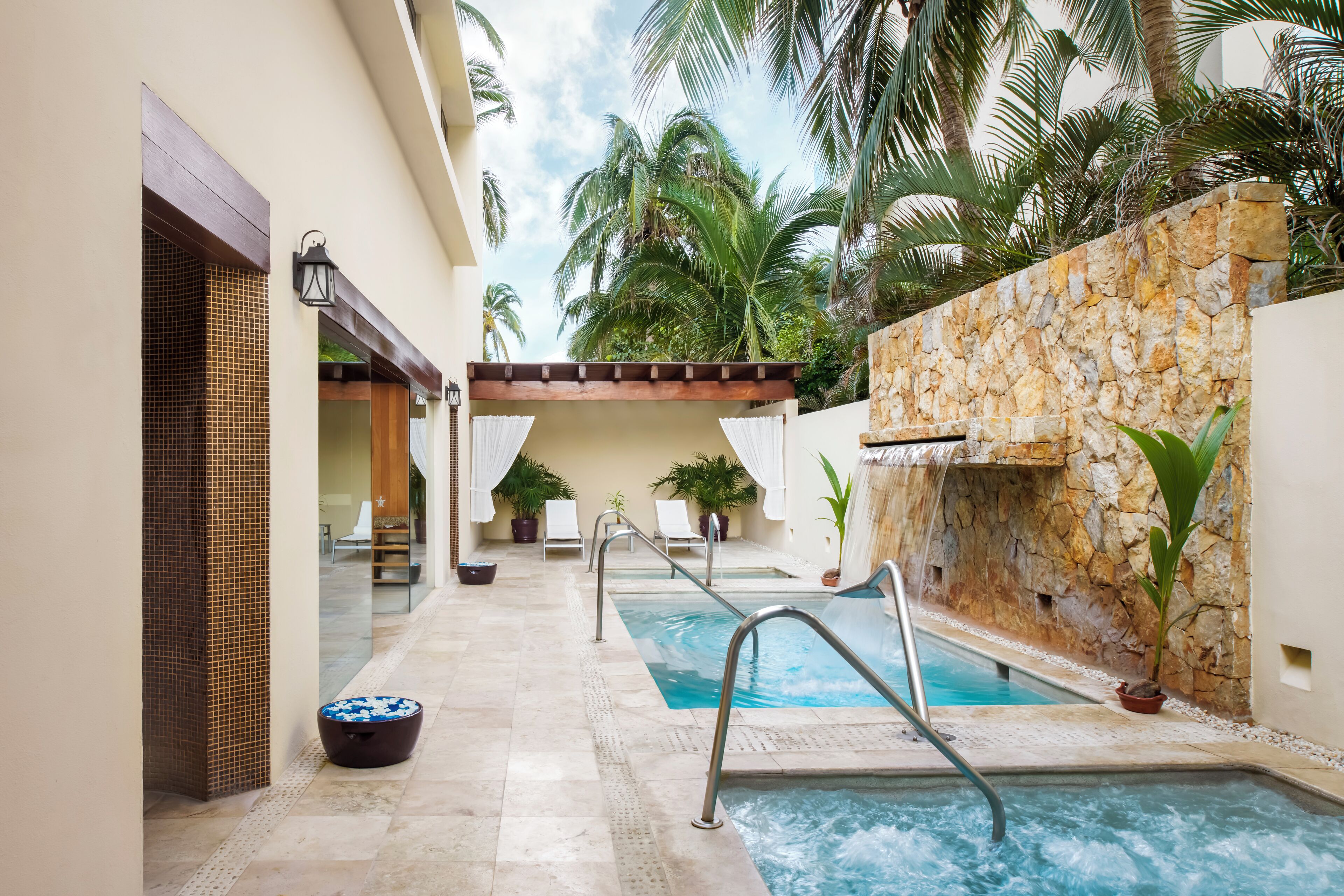Una piscina interior con pared de piedra, palmeras y suelo de baldosas.