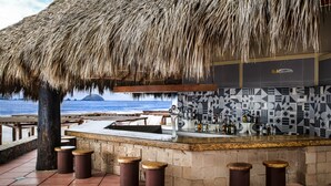 A beachside bar with a thatched roof, a tiled backsplash, and a view of the ocean.