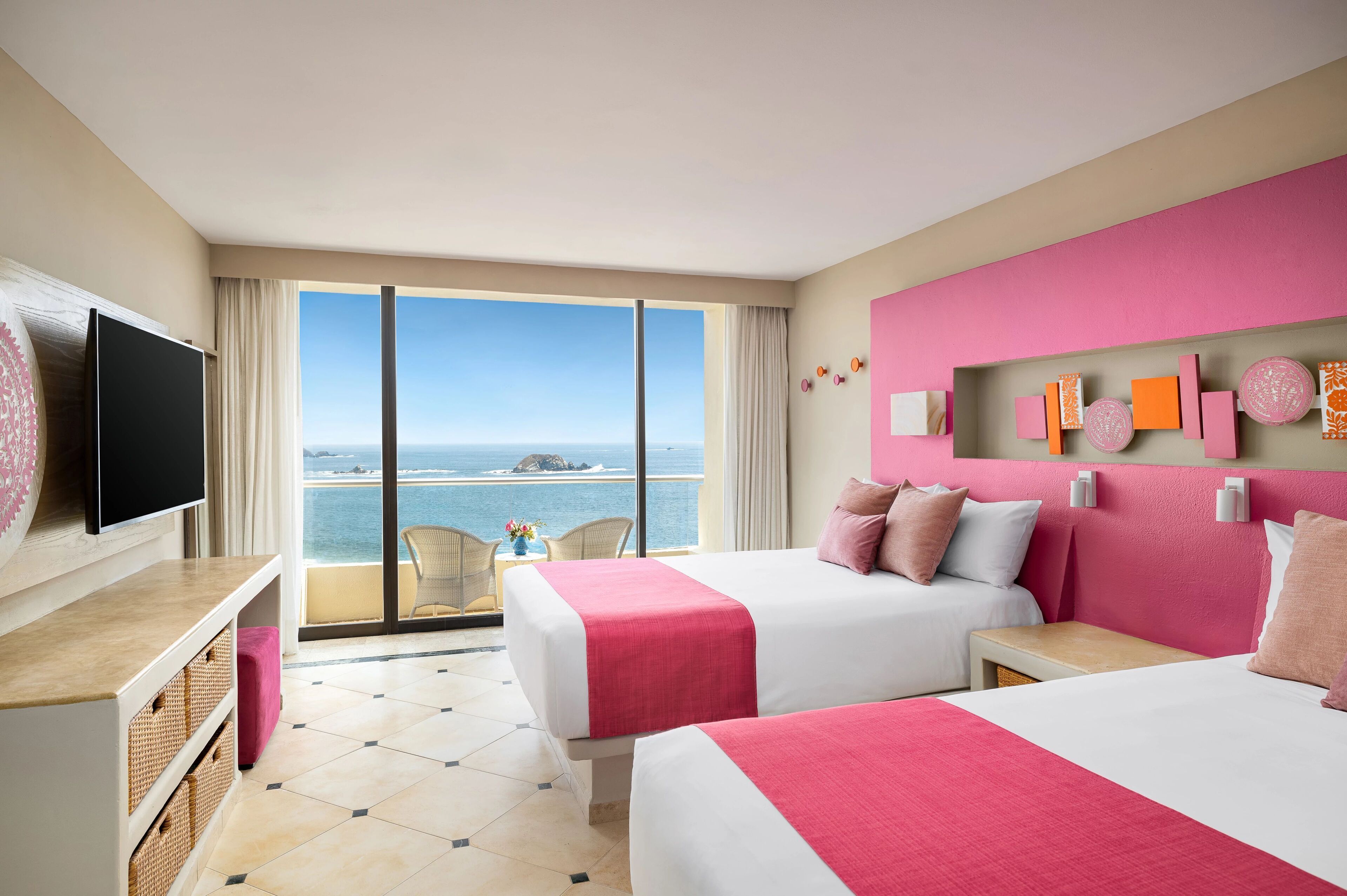 A hotel room with two beds, a TV, a balcony with a view of the sea, and decorative wall art.