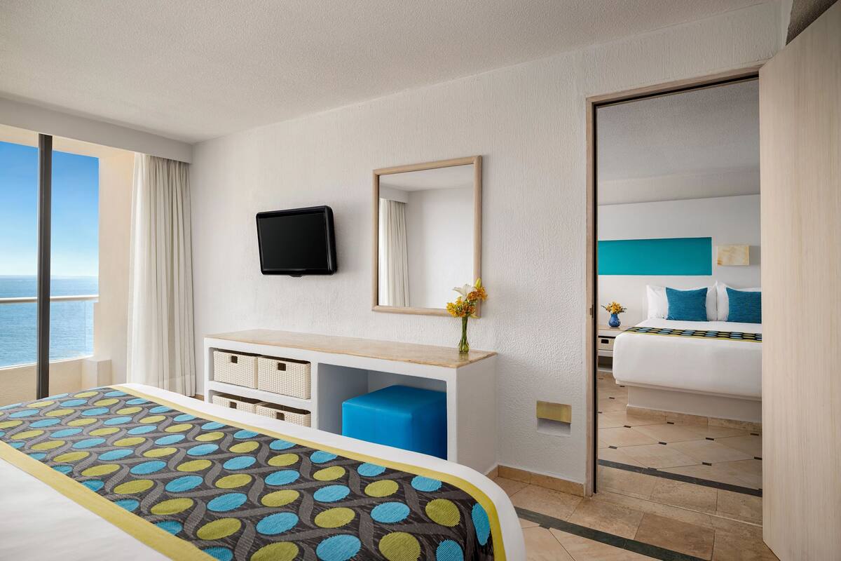 A hotel room with a large bed, a desk with a mirror, a television, and a view of the ocean.