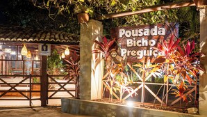 A sign for Pousada Bicho Preguiça with a rustic wooden structure and tropical plants. - Pousada Bicho Preguiça Pipa - RN (Tibau do Sul)