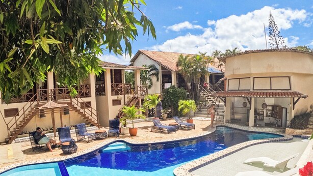 A swimming pool with a tiled edge, surrounded by lounge chairs and a covered seating area. - Pousada Bicho Preguiça Pipa - RN (Tibau do Sul)