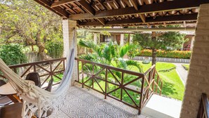A balcony with a hammock, a tiled floor, and a view of a garden with various plants and a pathway. - Pousada Bicho Preguiça Pipa - RN (Tibau do Sul)