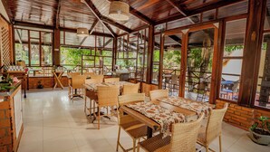 A spacious cafe with wicker furniture, large windows, and a tiled floor. - Pousada Bicho Preguiça Pipa - RN (Tibau do Sul)