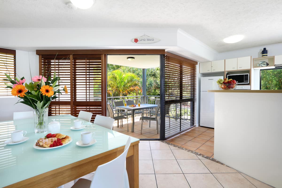 A modern kitchen with a dining area, a view of the garden, and a sign reading "Surfing Paradise".