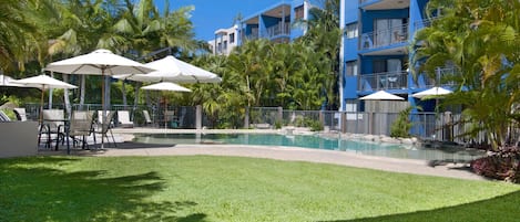 Zona de piscina con sombrillas, sillas y un césped bien cuidado.
