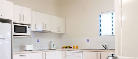 A modern kitchen with white cabinets, a microwave, a coffee maker, and a breakfast setting with croissants and coffee cups.