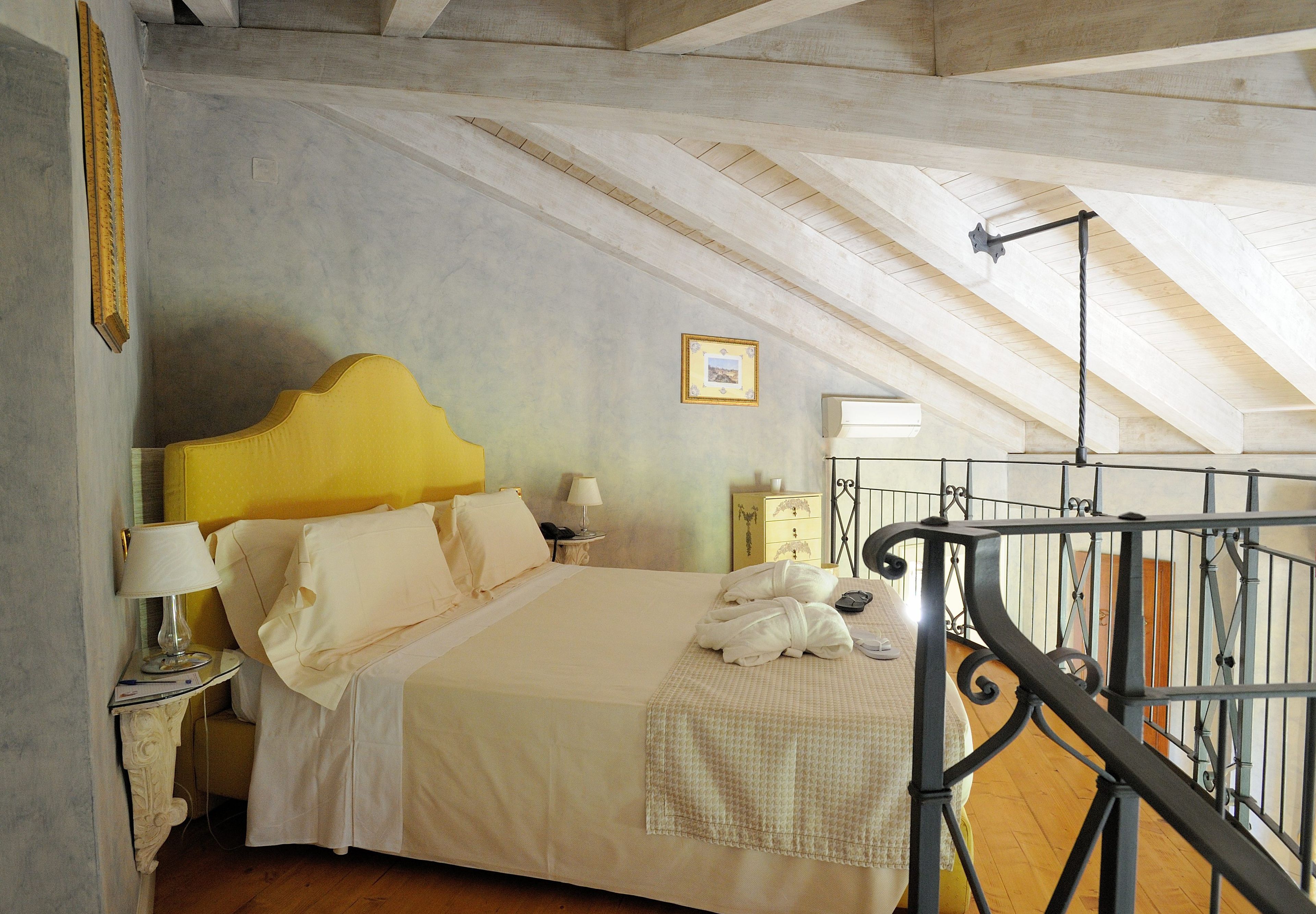 A bedroom with a bed, bedside tables, a lamp, a framed picture, and a staircase.