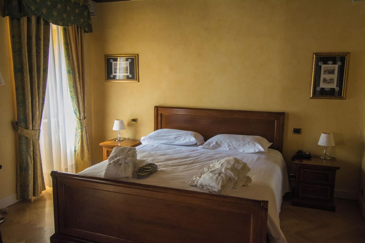 A neatly made bed with white linens and a wooden headboard, two bedside tables with lamps, and two framed pictures on the walls.