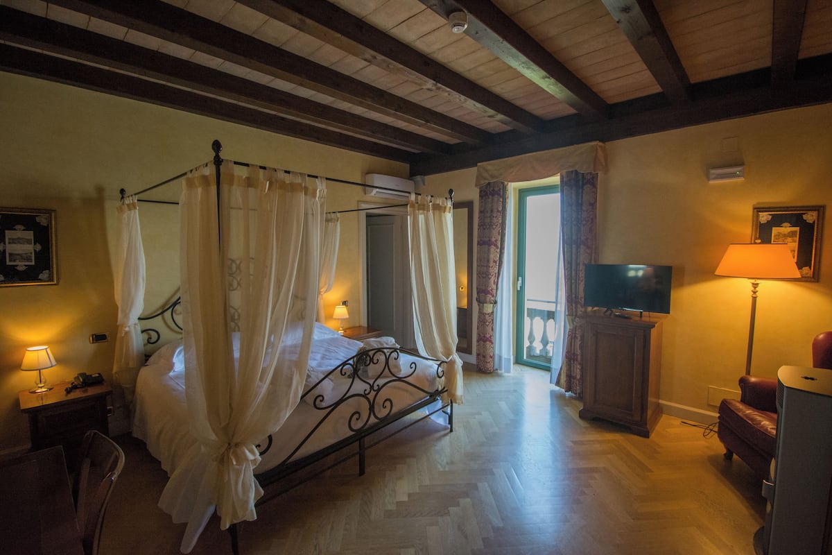 A bedroom with a four-poster bed, a television, a desk with a lamp, and a chair.