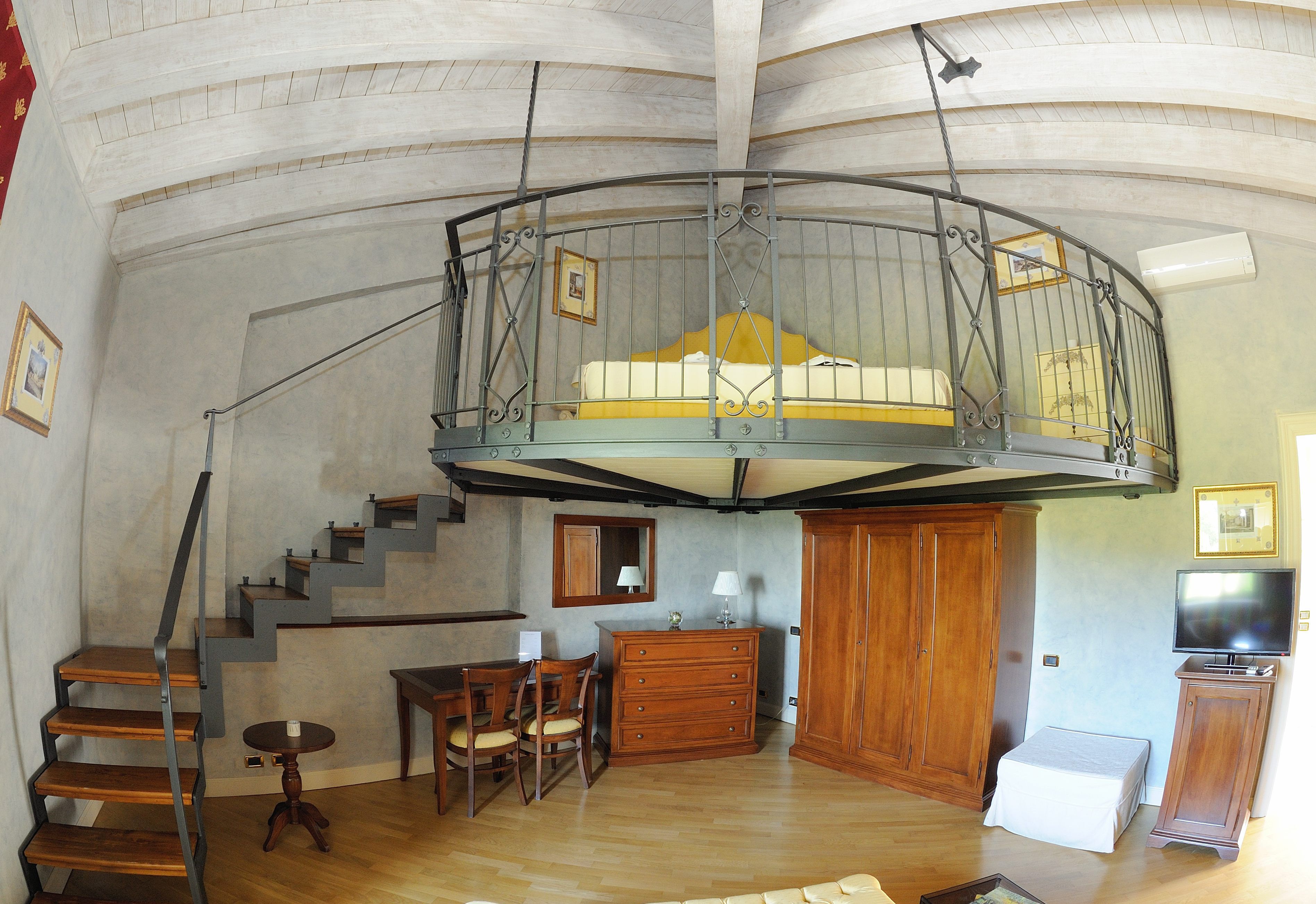 Un loft espacioso con un entrepiso con dormitorio, escalera de madera y televisor.