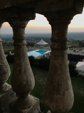 A view of a pool area with a tent, surrounded by greenery and a distant landscape.
