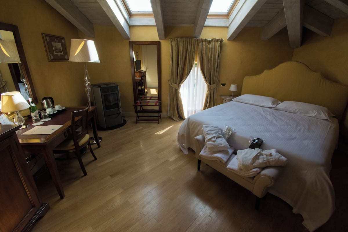 A hotel room with a bed, a desk with a lamp, a chair, a television, and a window with curtains.