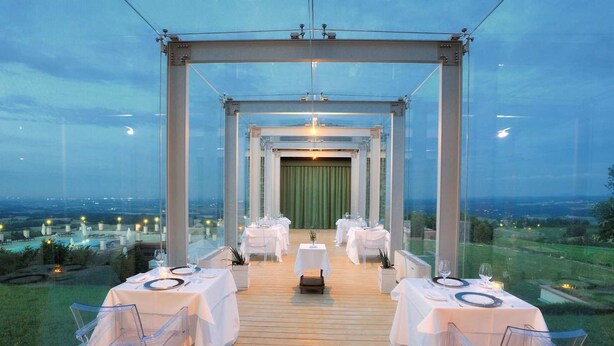 Un espace de restauration en plein air avec des tables dressées pour un repas, un fond de scène constitué d’un rideau vert et une vue sur le paysage.