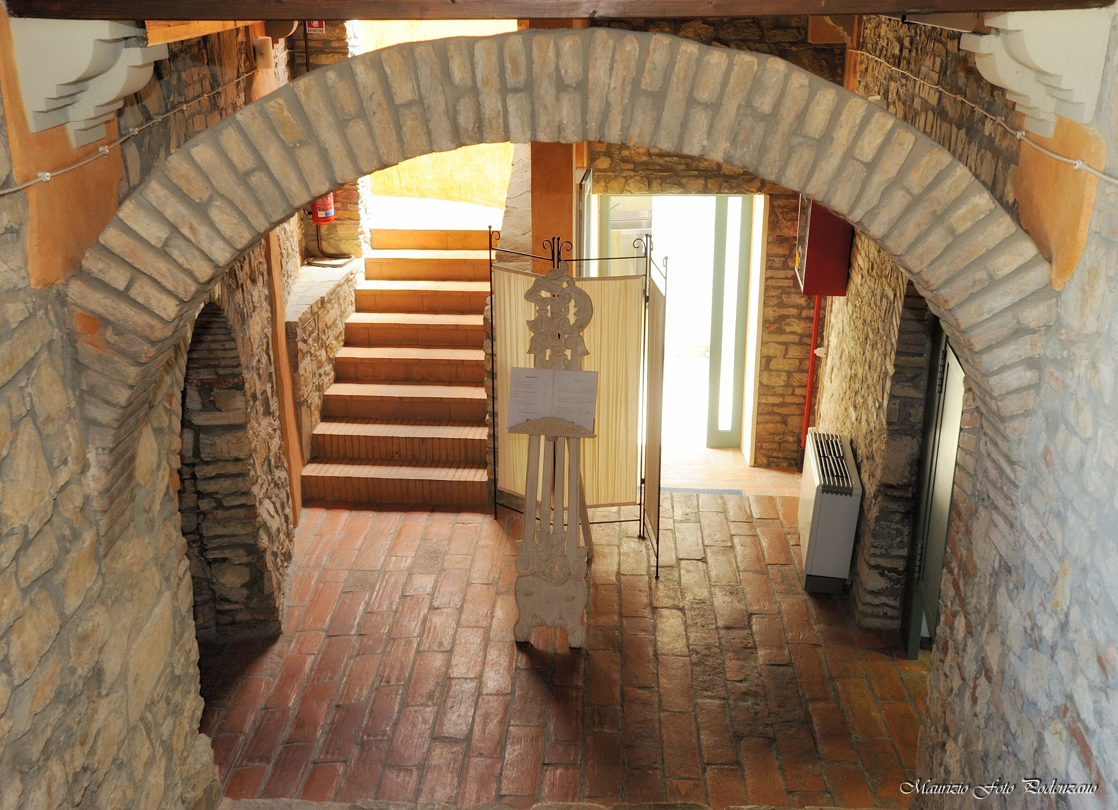 Un arc en pierre menant à un escalier doté d’une rampe en bois et d’une porte en métal.