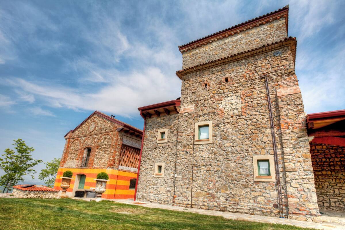 A stone building with a red roof and a smaller adjacent structure with a striped facade.