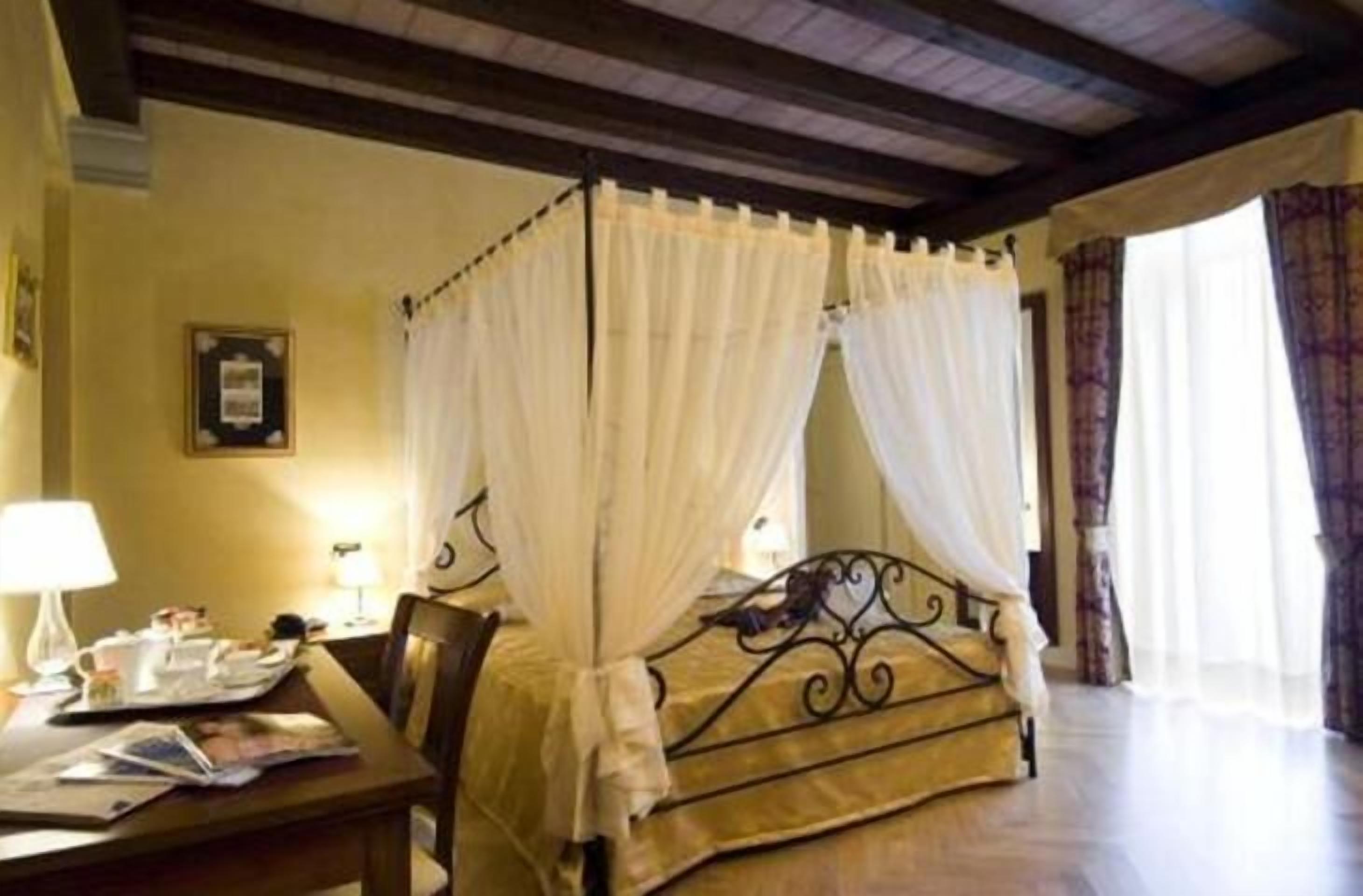 A bedroom with a four-poster bed, a bedside table with a lamp, and a window with curtains.