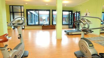 Uma academia com equipamentos de cardio, piso de madeira e grandes janelas.